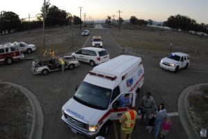 Car accident scene at rural intersection. Ambulance and fire trucks at the scene. Rescue workers talk to mother with two children.