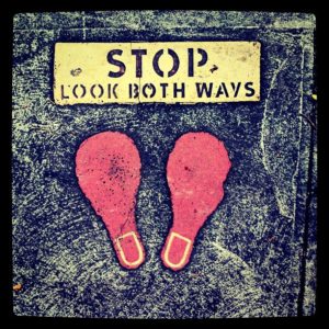 "Stop. Look both ways." sign on ground with red footprints highlights causes of pedestrian accidents.