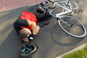 Bicycle accident. Biker lying on the road and holding his head.